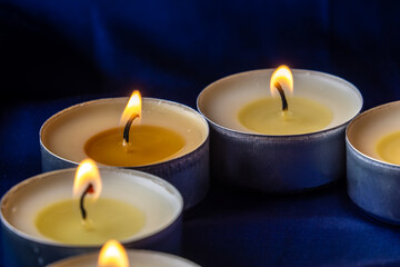Fototapeta na wymiar Round tea candles burn on a dark blue background. Wax melts in the candles.