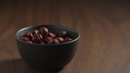 freeze-dried cranberries in black bowl on wood table with copy space