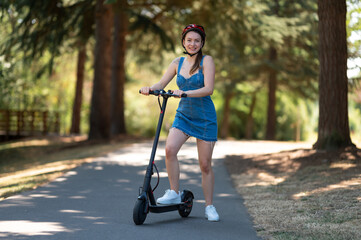 Active girl on an electric scooter in the park in summer. Beautiful nature, summer day. Big green...