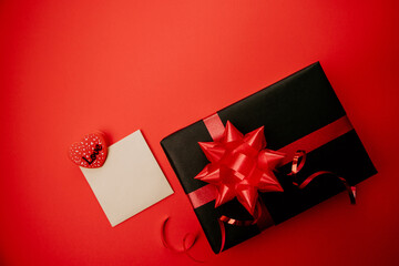 Valentine's Day design. Black gift box with red bows on a red background top view. Envelope, beige sheet with a clip with the inscription LOVE with space for text.
