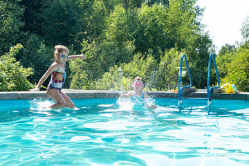 Two Caucasian girls aged 5-7 have fun swimming and splashing in the outdoor pool. Summer vacation in the backyard of the cottage.