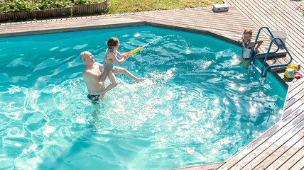 A middle-aged man and two Caucasian girls 5-7 years old swim and splash in the outdoor pool. Summer vacation in the backyard of the cottage.