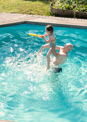 A middle-aged man and a 5-year-old Caucasian girl have fun swimming and splashing in an outdoor pool. Summer vacation in the backyard of the cottage.