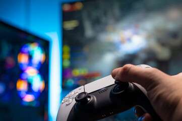 Gamepad in the hand of a gamer. Large screen TV. macro photography. Neon lighting. Cybersport, gaming, fun, online video games with friends, youth culture, gambling business, game strategy.