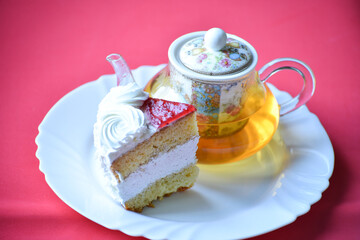 Green tea in teapot and peace of buscuit cake on pink background, tea ceremony. Sweets to eat and drink, birthday party set