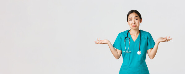 Covid-19, healthcare workers, pandemic concept. Portrait of clueless asian female nurse, woman doctor shrugging and spread hands sideways unaware, dont know, cant help, white background - obrazy, fototapety, plakaty