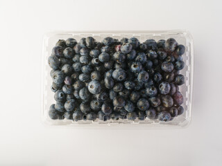 Lots of fresh blueberries in a plastic shopping container. Agriculture and forestry, harvest, supermarket, vitamins, antioxidants, gastronomy, cooking. Plain white background.