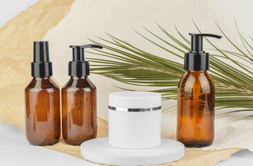 Cosmetic bottles with dispensers and a white jar of moisturizer on a beige background with palm leaves. SPA products
