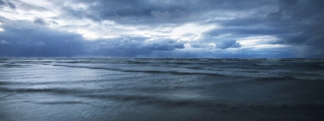 Dark storm sky above the Baltic sea, waves and water splashes. Dramatic cloudscape. Nature, environment, fickle weather, climate change. Atmospheric scenery. Panoramic view, long exposure