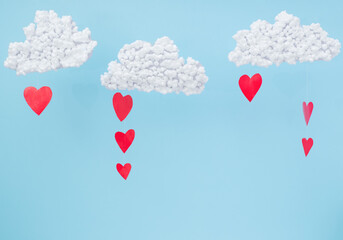 Fototapeta na wymiar White clouds and red paper hearts in the form of rain on a blue background. Abstract background with paper-cut shapes. Sainte Valentine, mother's day