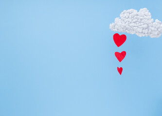 Fototapeta na wymiar White clouds and red paper hearts in the form of rain on a blue background. Abstract background with paper-cut shapes. Sainte Valentine, mother's day