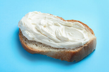 Slice of bread with tasty cream cheese on light blue background, closeup