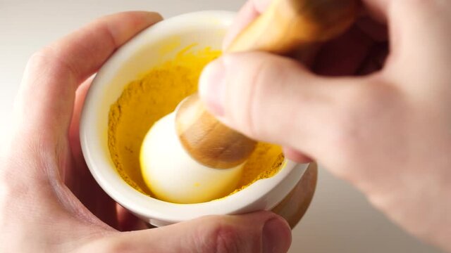 Top view of a pestle mixing finely grounded spices in the white ceramic mortar. Man hands grind the spices with a mortar.
