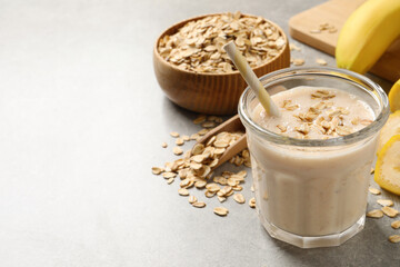 Glass of tasty banana smoothie with oatmeal on light grey table. Space for text