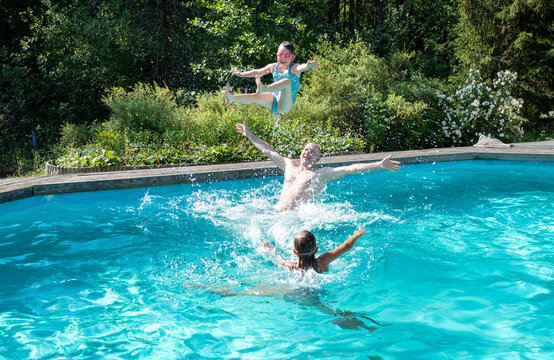 Caucasian girls 5 years old and their middle-aged father happily splash and dive in the outdoor pool. Summer vacation in the backyard of the cottage.