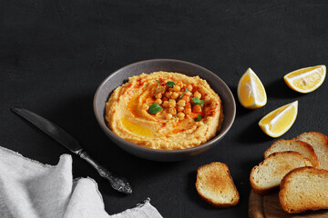 bowl of hummus with paprika on dark table with pieces of lemon and bread . copy space