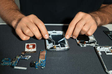 Technician repairing broken smartphone at table, closeup