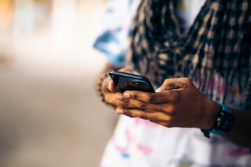 Detail of the hands of a black man leaning against a wall using his smartphone.