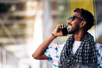 Close up of a smiling black man leaning against a glass wall using his smartphone in profile