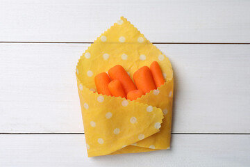 Many baby carrots in beeswax food wrap on white wooden table, top view