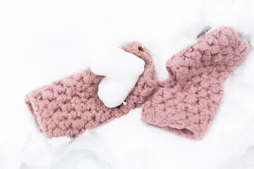 Pink knitted gloves with heart of snow in winter day. Love concept.