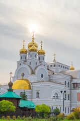 Christian temple with golden domes and crosses against a cloudy sky and trees with green foliage 