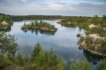 Fototapeta na wymiar An old granite quarry and a formed lake with a sandy-rocky shore and tree-covered islands.
