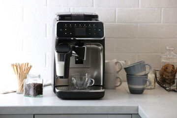 Modern electric coffee machine with glass cup on white marble countertop in kitchen