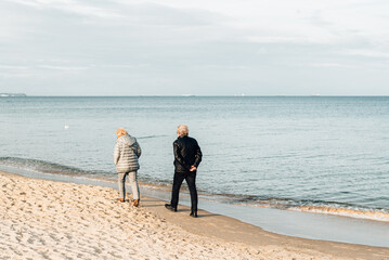 Elderly couple walks along the shore of the cold sea. Love in old age. Travel to Scandinavia.