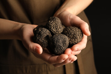 Woman holding heap of truffles in hands on black background, closeup