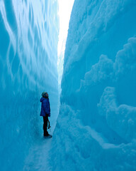 Adventurous Girl Ice Climbing in Slot Canyon on Blue Matanuska Glacier in Alaska. Glacier is receding and melting due to global warming. Ice climbing equipment is visible. - obrazy, fototapety, plakaty