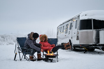 Travelers Adventure Couple sitting around campfire and Airstream RV Travel Trailer Camper in the...