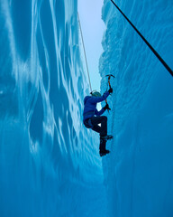 Adventurous Girl Ice Climbing in Slot Canyon on Blue Matanuska Glacier in Alaska. Glacier is receding and melting due to global warming. Ice climbing equipment is visible.
