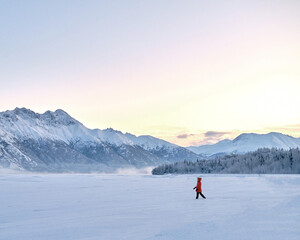 Girl wearing parka and walking in a snowy landscape in Alaska during winter. Gorgeous sunrise and colorful mountains in background with lots of snow © Collin