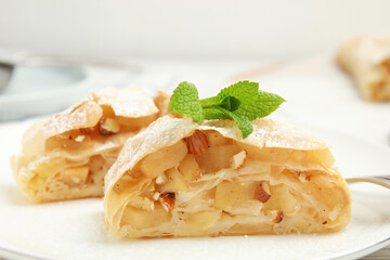 Pieces of delicious apple strudel with almonds, powdered sugar and mint on plate, closeup