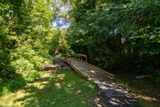 A suburban trail walkway with a wooden bridge over a creek.