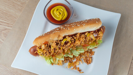 Hot dog with lettuce, gherkin, fried onions, ketchup on white plate. Hot dog prepared with danish ingredients.