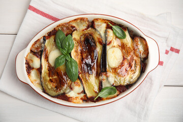 Delicious eggplant lasagna in baking dish and napkin on white wooden table, top view