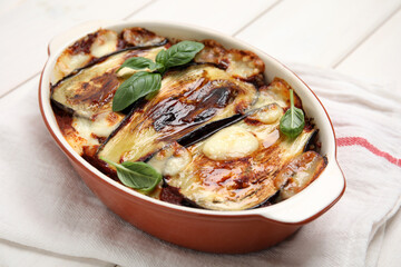 Delicious eggplant lasagna in baking dish and napkin on white wooden table, closeup
