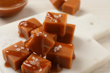 Tasty caramel candies with sauce and sea salt on white table, closeup