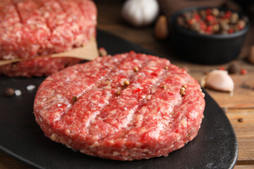 Raw hamburger patties with pepper on black board, closeup