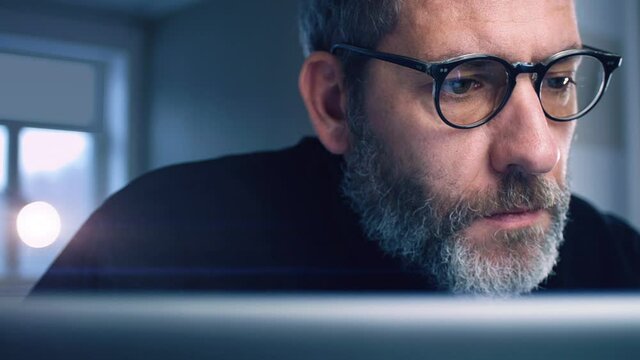 Portrait of a businessman with glasses working concentrated with his computer in home office - slow tracking shot
