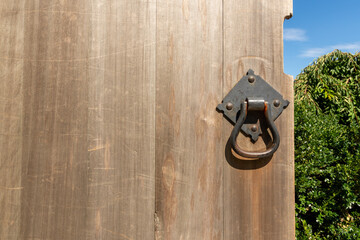 A close up of a weathered wooden door with an iron door handle that opens into a garden. Copy space. Horizontal orientation.