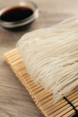 Dried rice noodles with soy sauce on wooden table, closeup