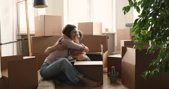 Happy playful little 5s daughter jumping out cardboard box hugs parents, enjoy playtime with loving mom and dad, homeowners family celebrate relocation day to own first house. Move day, tenant concept