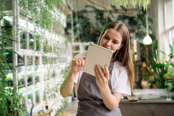 The florist works in the studio of flowers and plants for the house. Uses tablet internet information.