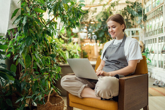 A florist entrepreneur works in a studio of flowers and plants for the home. Gardener woman uses laptop internet information.