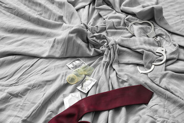 Male necktie and condoms with handcuffs on bed after romantic date - obrazy, fototapety, plakaty
