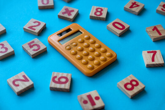 Calculator and a wooden number and mathematical symbol on blue background.