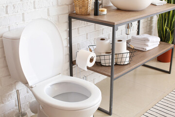 Toilet bowl and basket with rolls of paper near white brick wall